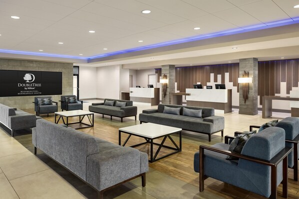 A hotel lobby with seating areas, a reception desk, and a wall-mounted sign.