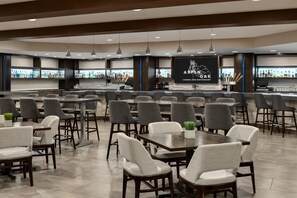 A modern bar area with multiple seating options, a counter with a menu display, and a variety of bottles and glasses.
