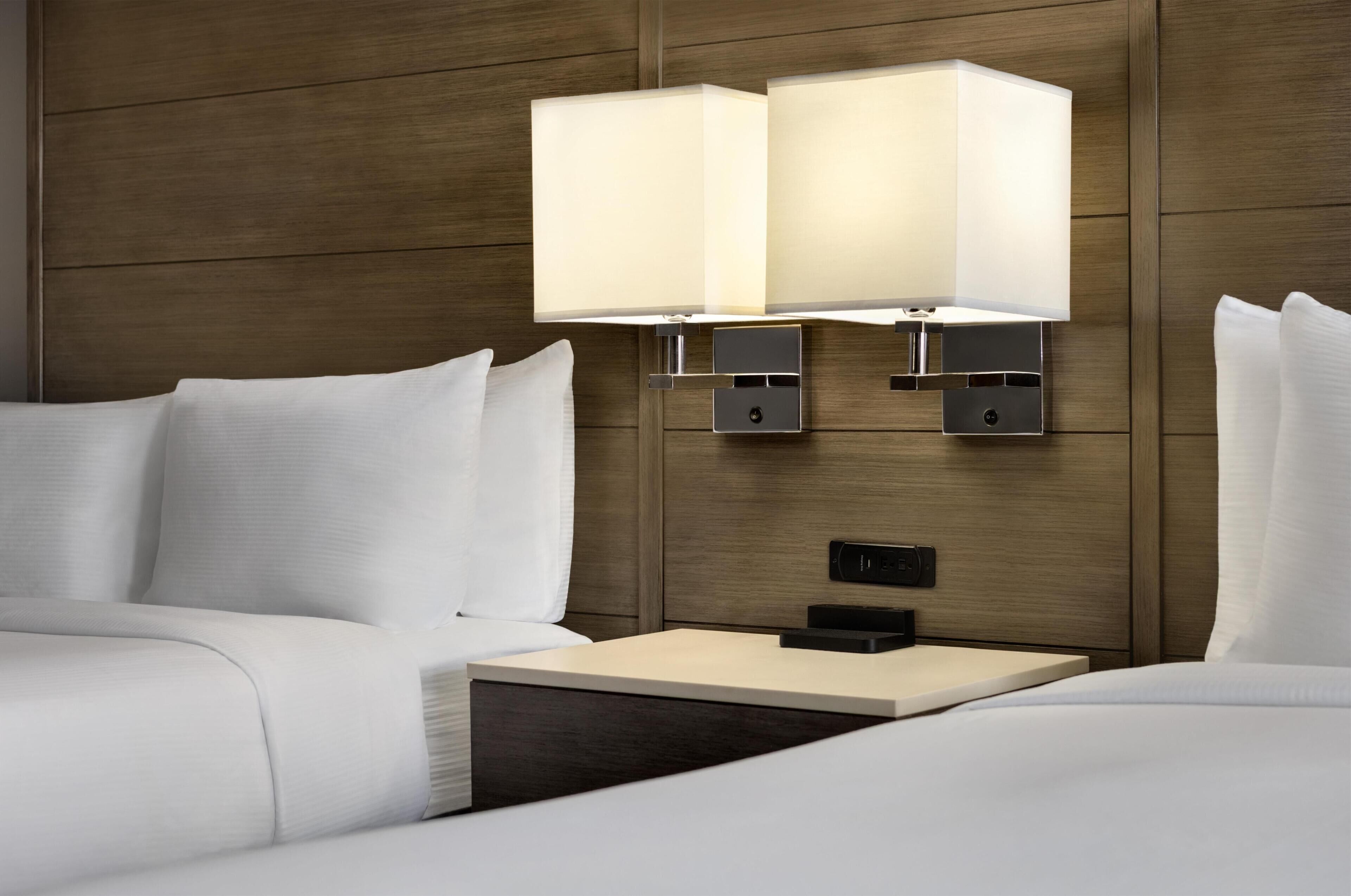 Quarto de hotel com cama, mesa de cabeceira e luminária na parede.