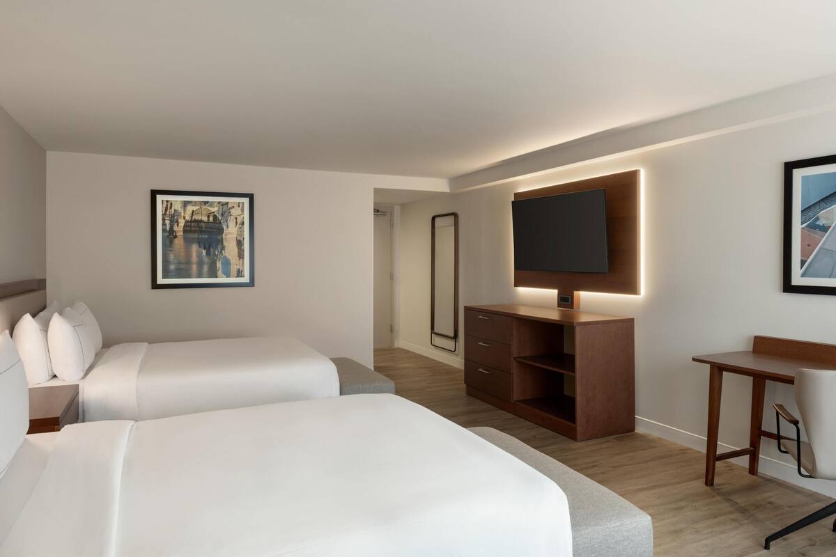 Een moderne hotelkamer met twee bedden, een bureau, een spiegel en een televisie.