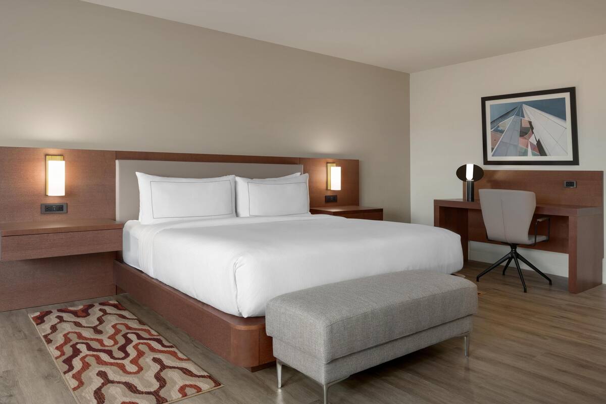 Een moderne hotelkamer met een groot bed, nachtkastjes, een bureau met een stoel en een aan de muur hangend schilderij.