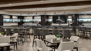 A modern bar area with a bar counter, seating, and a large screen displaying the name "Aspen Oak Lounge and Restaurant". - Doubletree by Hilton Bloomington - Minneapolis South (Bloomington)