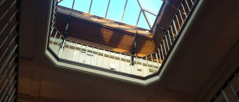 Ein Blick auf ein Oberlicht mit geometrischem Glasmuster, eine Holzbalkendecke und ein Metallgeländer.