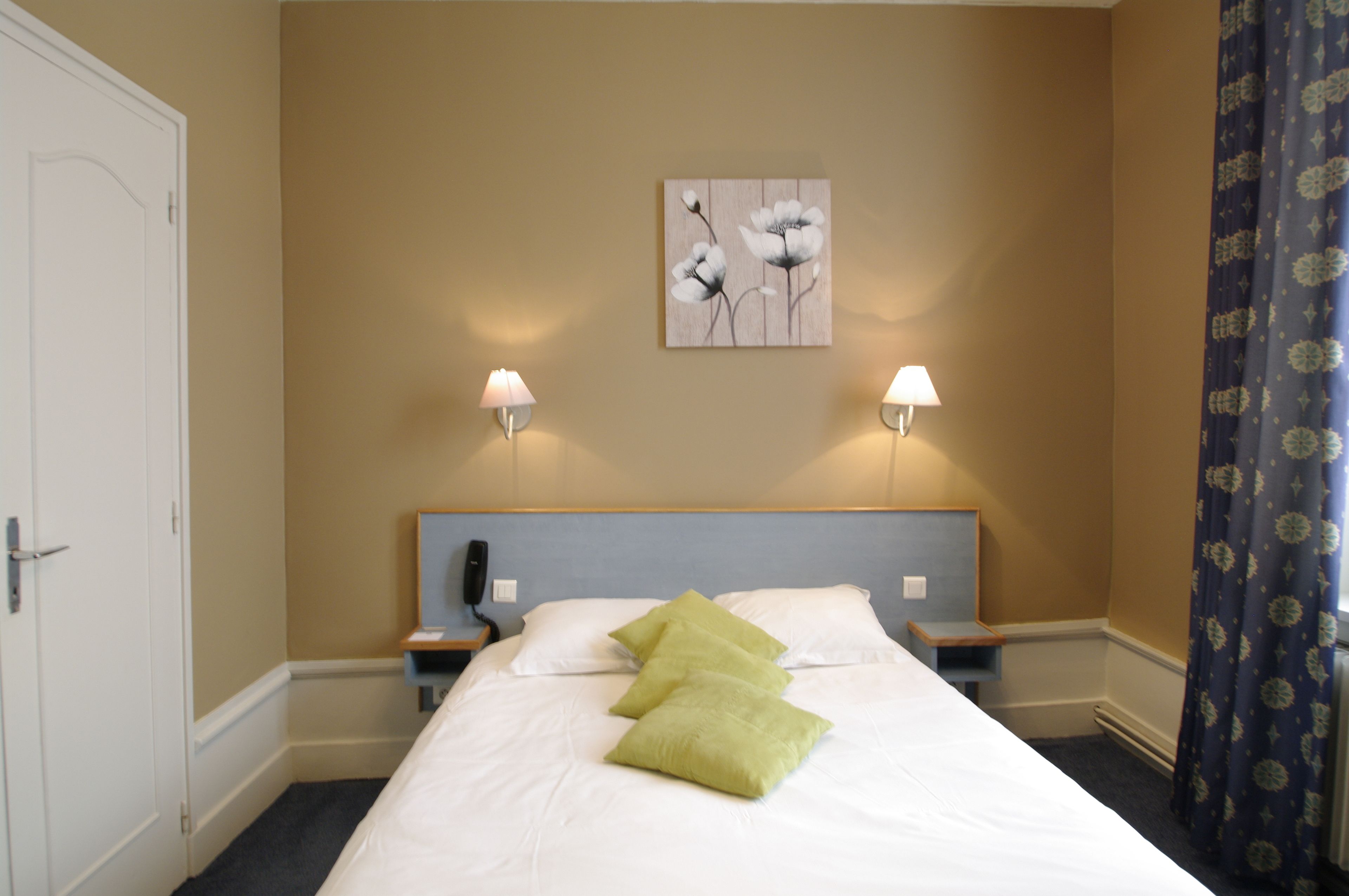 Habitación de hotel con cama, dos lámparas de noche, mesitas de noche, teléfono y un cuadro en la pared.