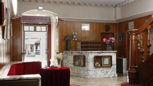 Eine Lobby mit einer Rezeption, einem roten Sofa, einem Marmor-Empfangsbereich und einer Holztreppe.