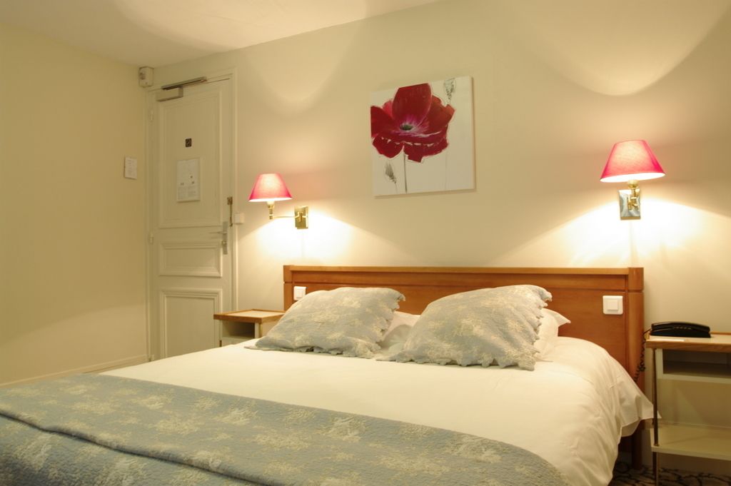 A neatly made bed with a blue blanket, two bedside lamps, a wooden headboard, and a red flower painting on the wall.