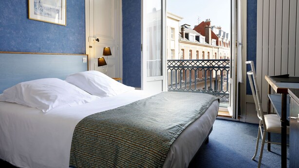 Ein Hotelzimmer mit einem Bett, einem Schreibtisch und Blick auf Gebäude durch eine offene Tür.