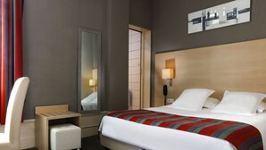 Ein Hotelzimmer mit einem Bett, einem Schreibtisch, einem Sessel, einem kleinen Hocker, einem Spiegel, einem an der Wand montierten Telefon und einer Tür.