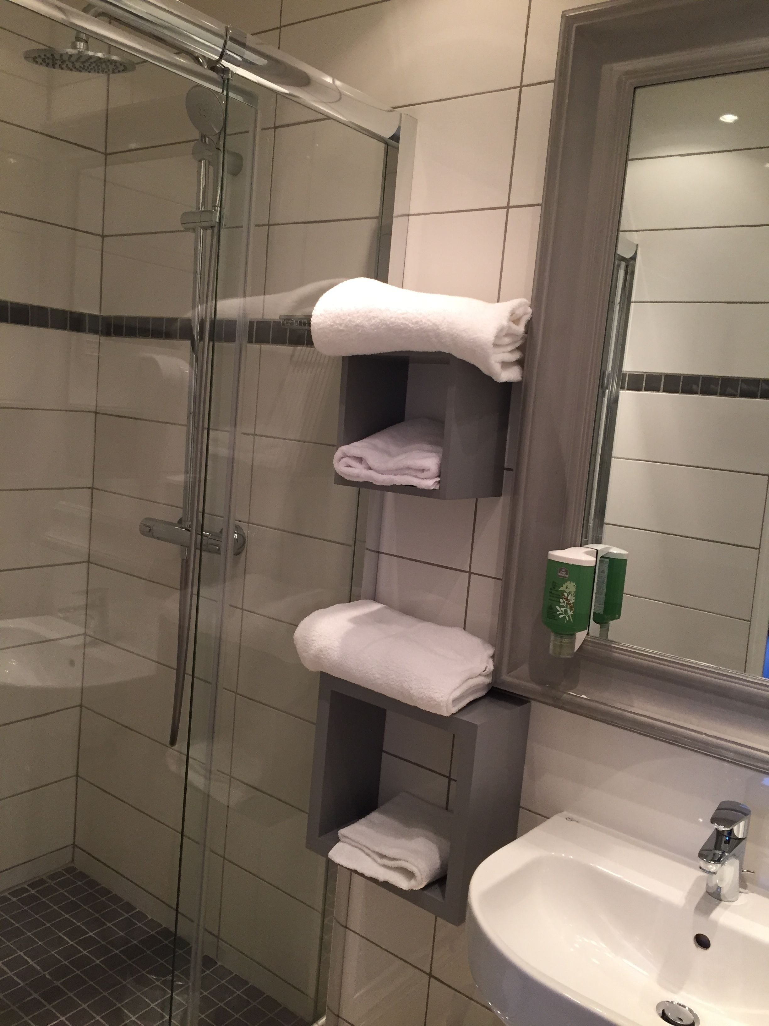 A bathroom with a glass-enclosed shower, a white sink, and multiple shelves holding folded towels.