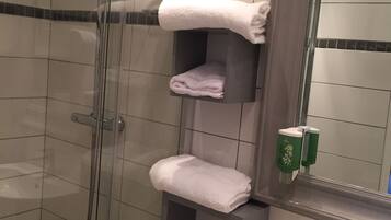 A bathroom with a glass-enclosed shower, a white sink, and multiple shelves holding folded towels.