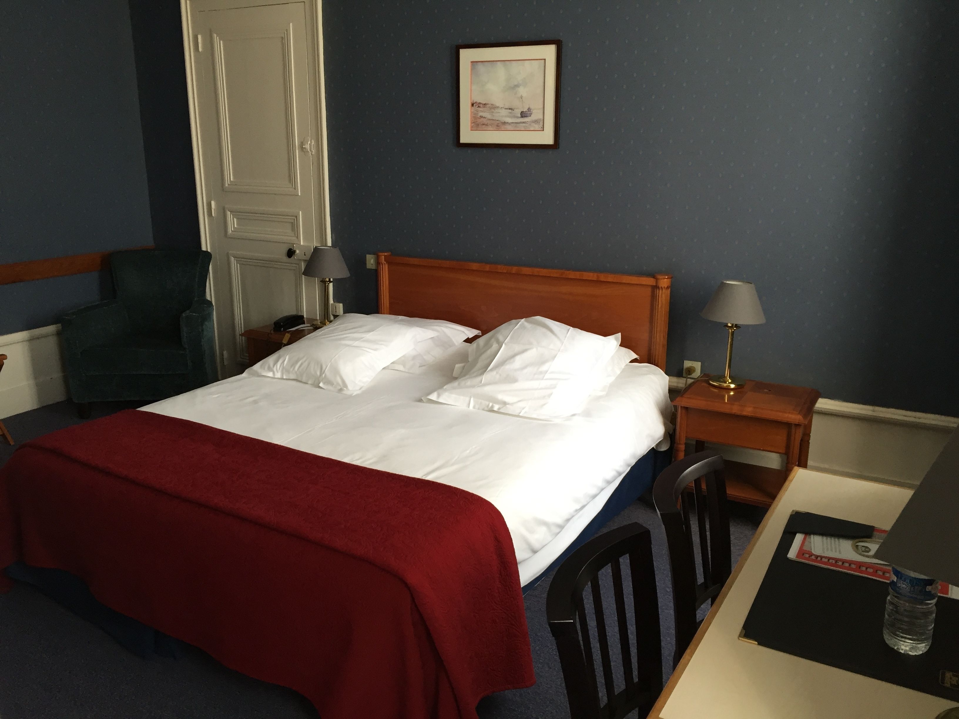 Habitación de hotel con cama, escritorio, silla, lámpara y un cuadro en la pared.