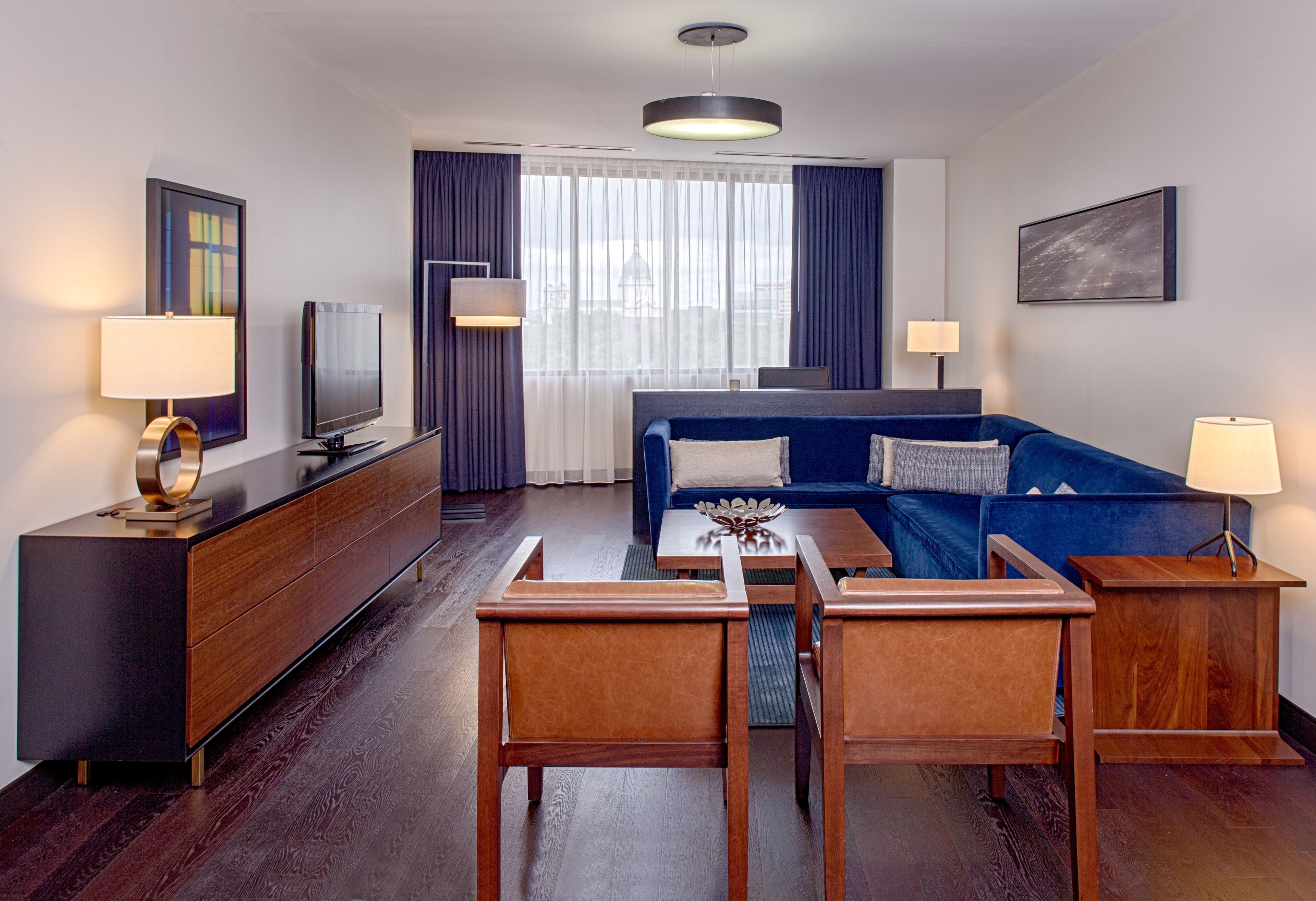 Una habitación de hotel moderna con un sofá, dos mesitas de madera, un televisor y un escritorio con cajones.