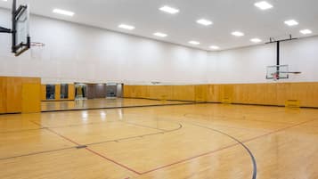 A large indoor basketball court with wooden flooring, two basketball hoops, and a wooden wall with a mirror.