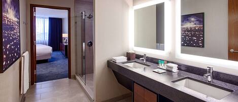 A hotel bathroom with a large mirror, two sinks, and a shower area.