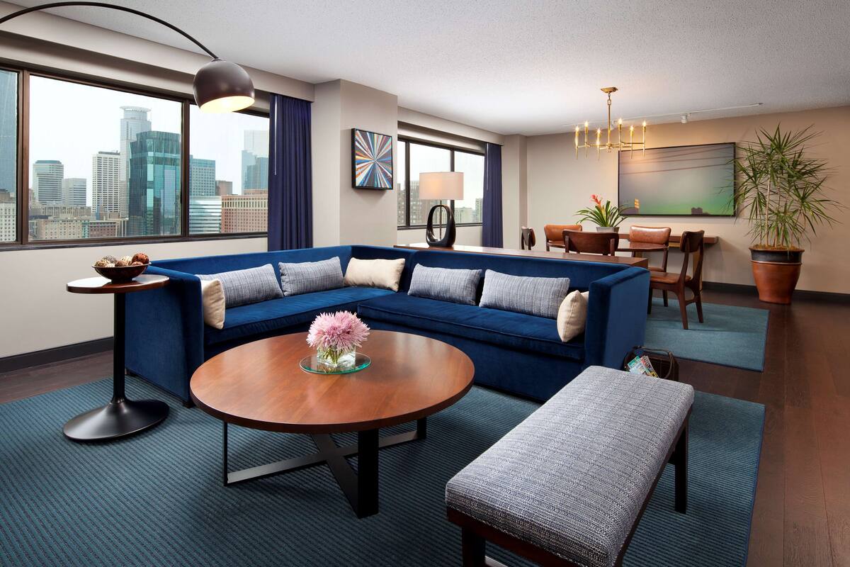 A modern living room with a blue sectional sofa, a round coffee table, and a view of the city skyline through large windows.