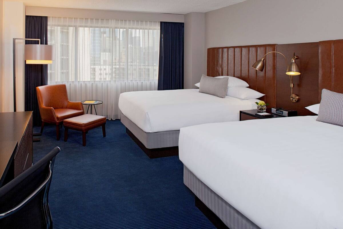 A hotel room with two beds, a desk with a TV, a chair, and a small table.