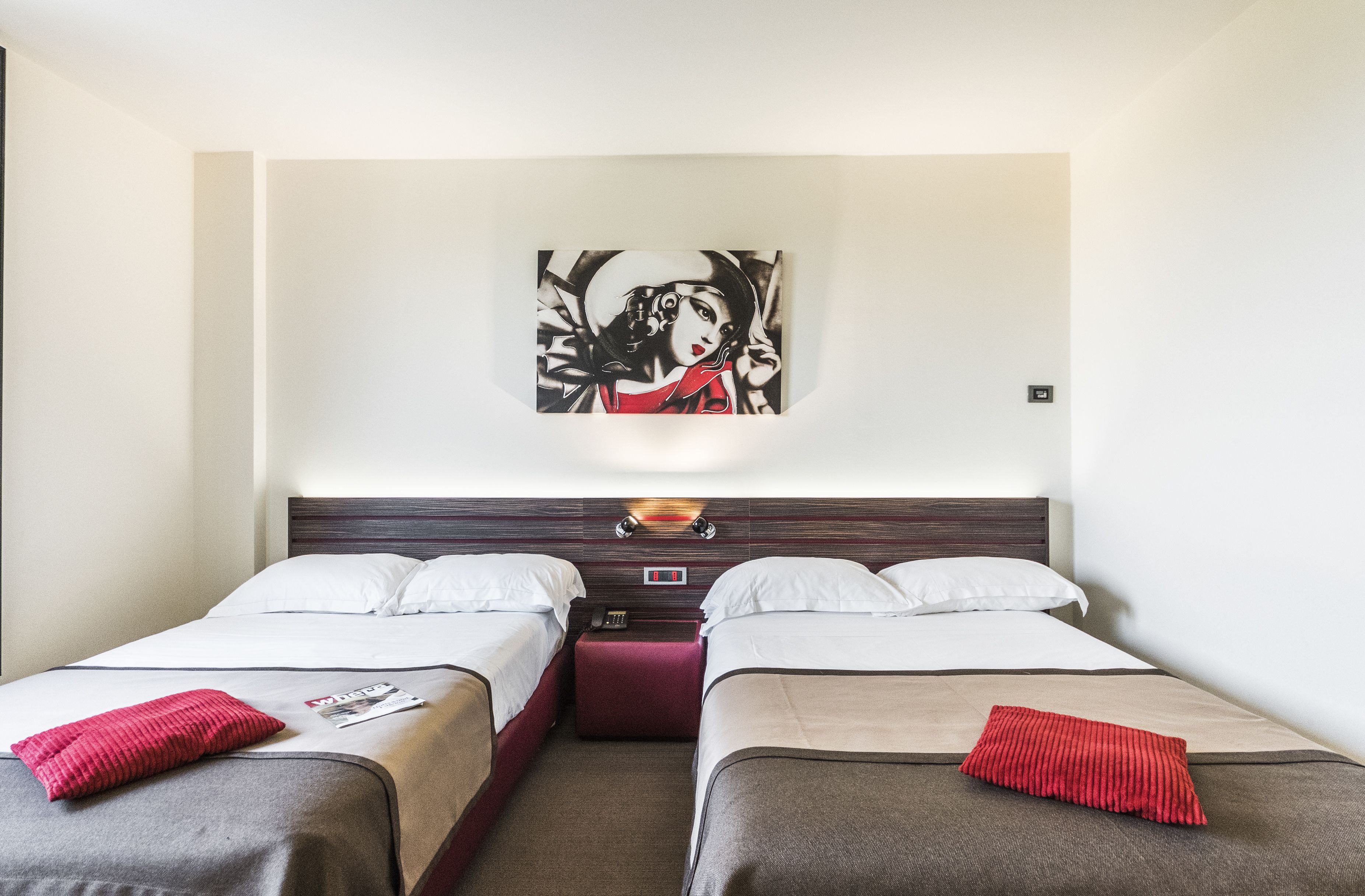 Ein Hotelzimmer mit zwei Betten, einem Nachttisch, einem Wandbild und einem Beistelltisch mit Lampe.
