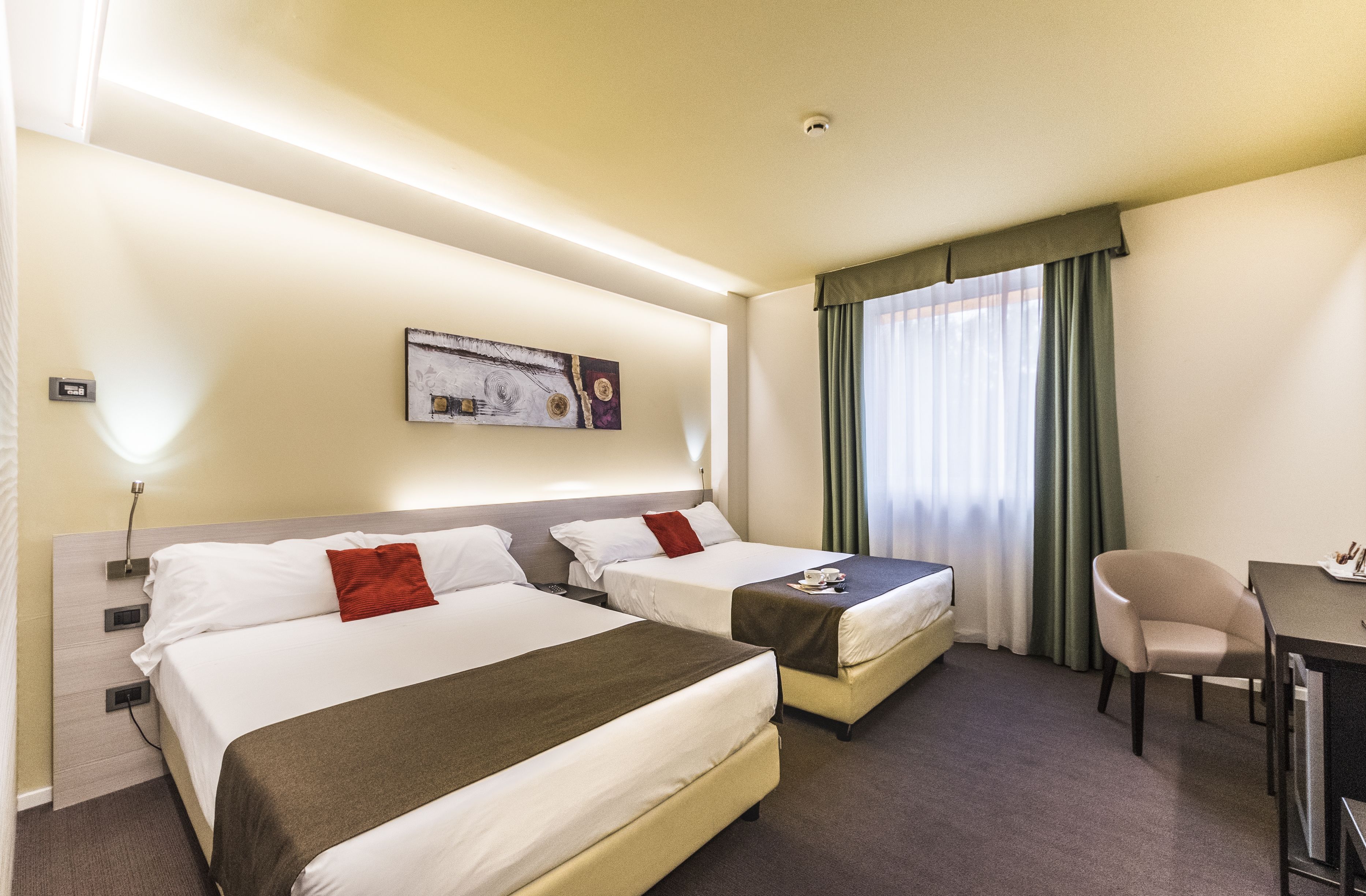 Una habitació d'hotel amb dos llits, una escriptori, una cadira, un quadre a la paret i una finestra amb cortines.
