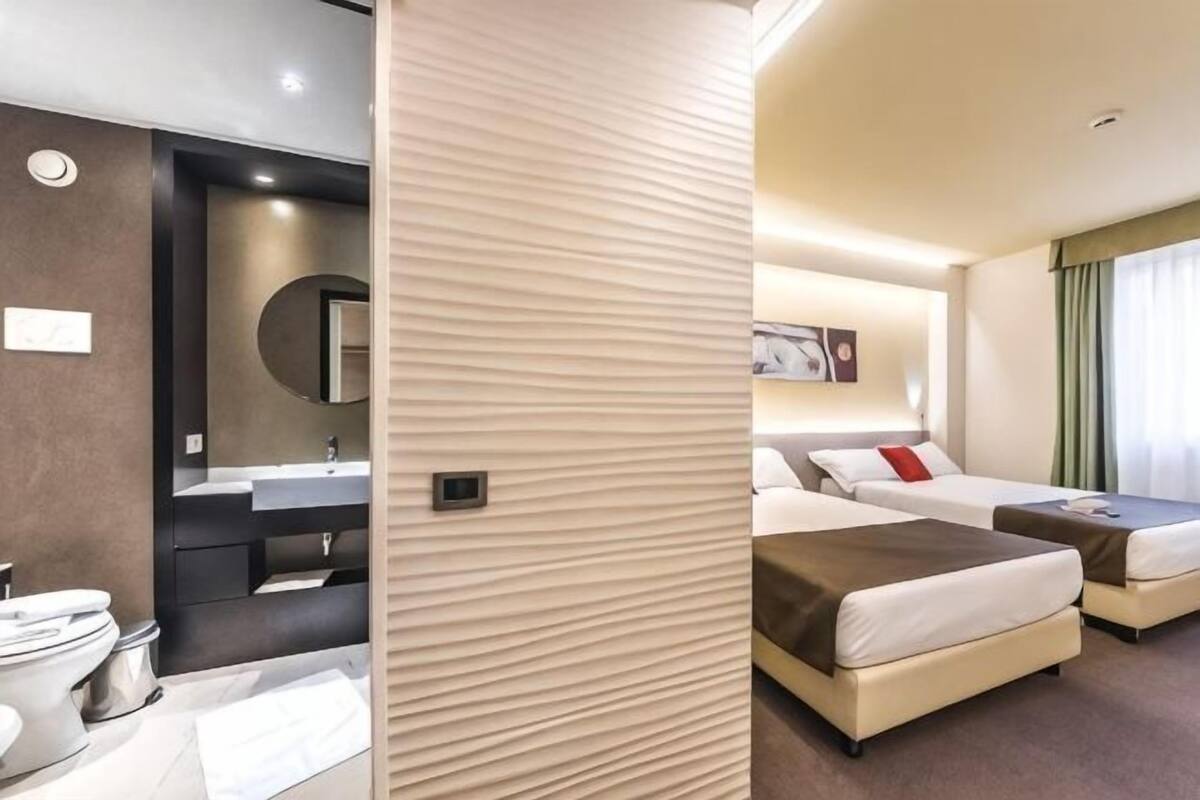 A hotel room with a bathroom, two beds, a mirror, and a sink.