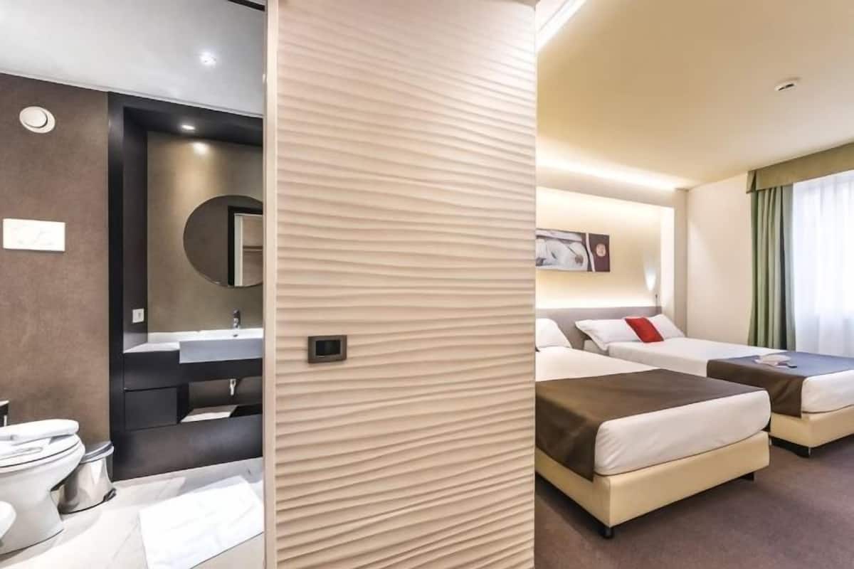 Ein Hotelzimmer mit Bad, zwei Betten, einem Spiegel und einem Waschbecken.