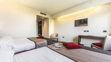 Habitación de hotel con dos camas, un escritorio, una silla, un televisor y una revista sobre la cama.