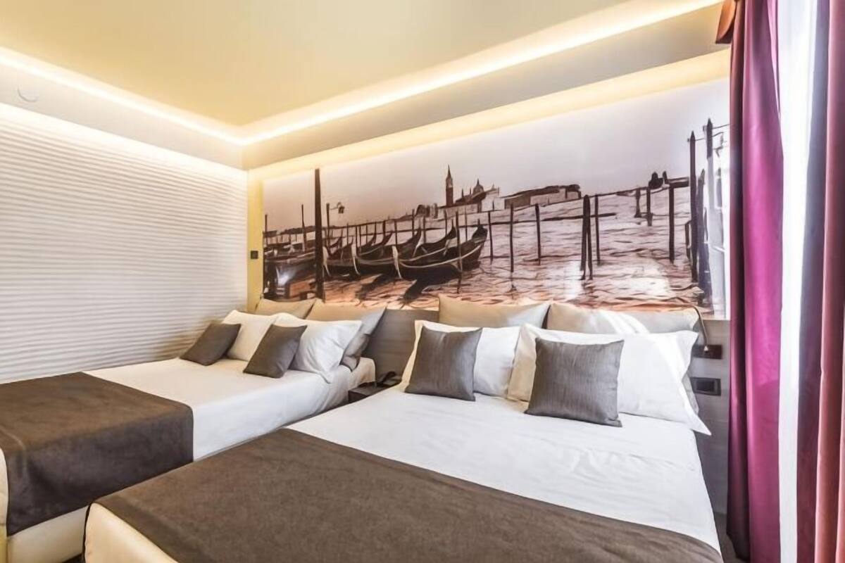 A hotel room with two beds, a mural of a canal scene, and a window with curtains.