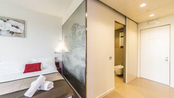 A hotel room with a bed, a painting, a bathroom, and a door.