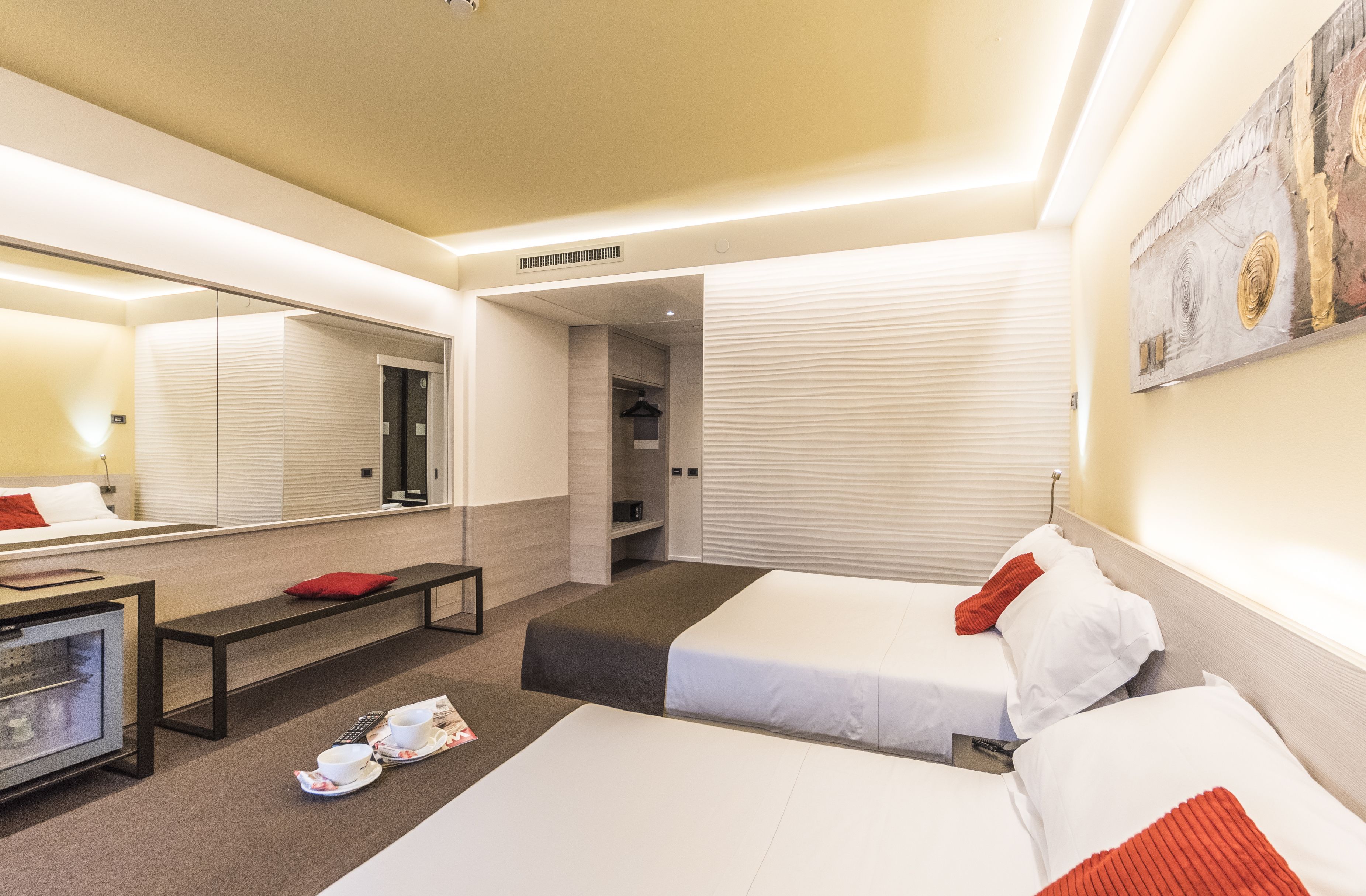 Habitación de hotel con dos camas, un escritorio con computadora, un espejo y un cuadro en la pared.