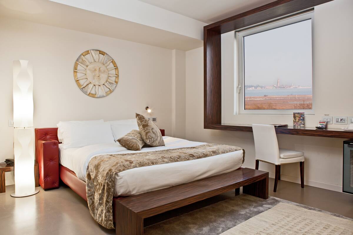 A bedroom with a large bed, a desk, and a view of the sea.