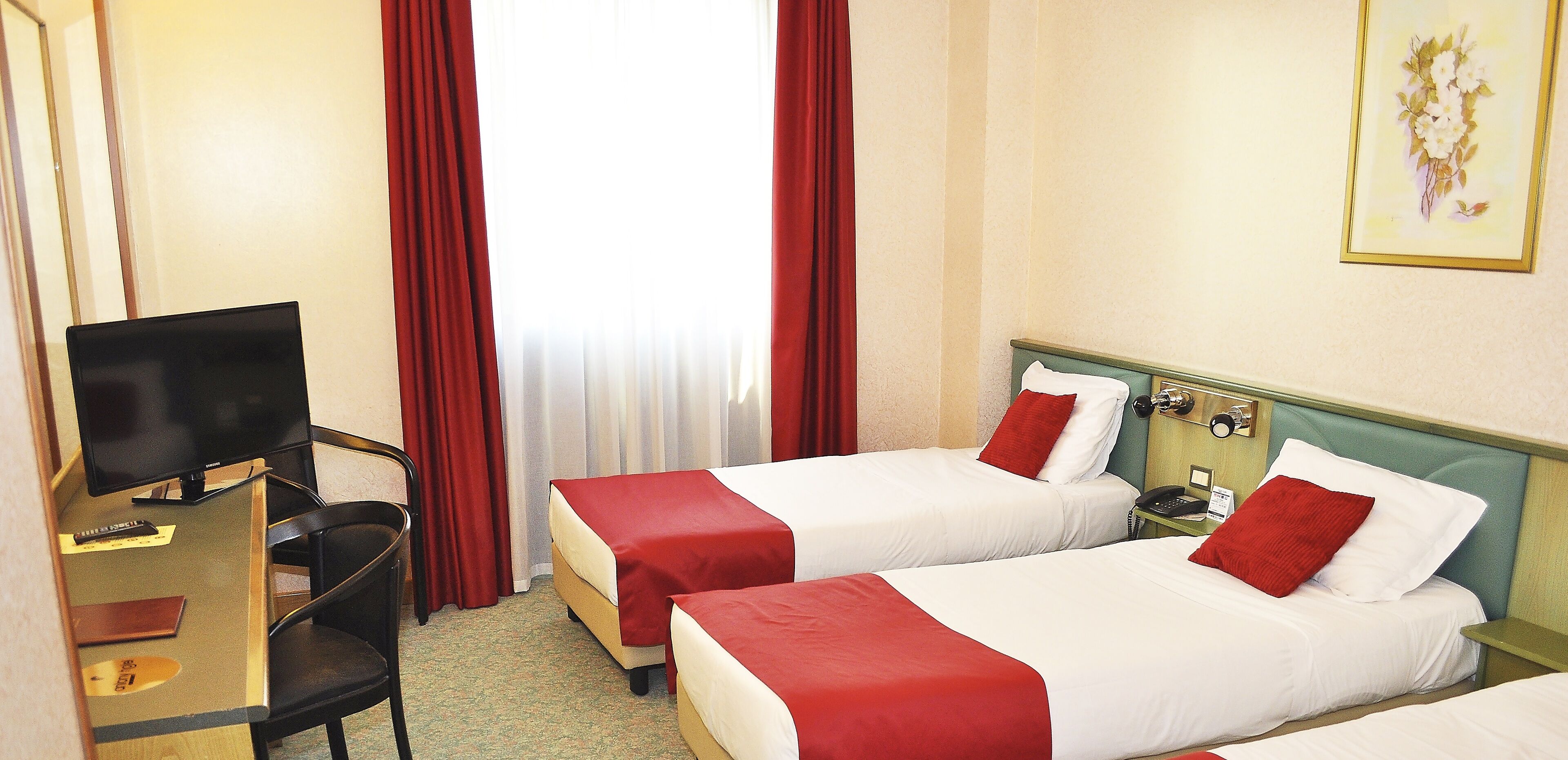 A hotel room with two beds, a desk with a television, and a nightstand with a phone.