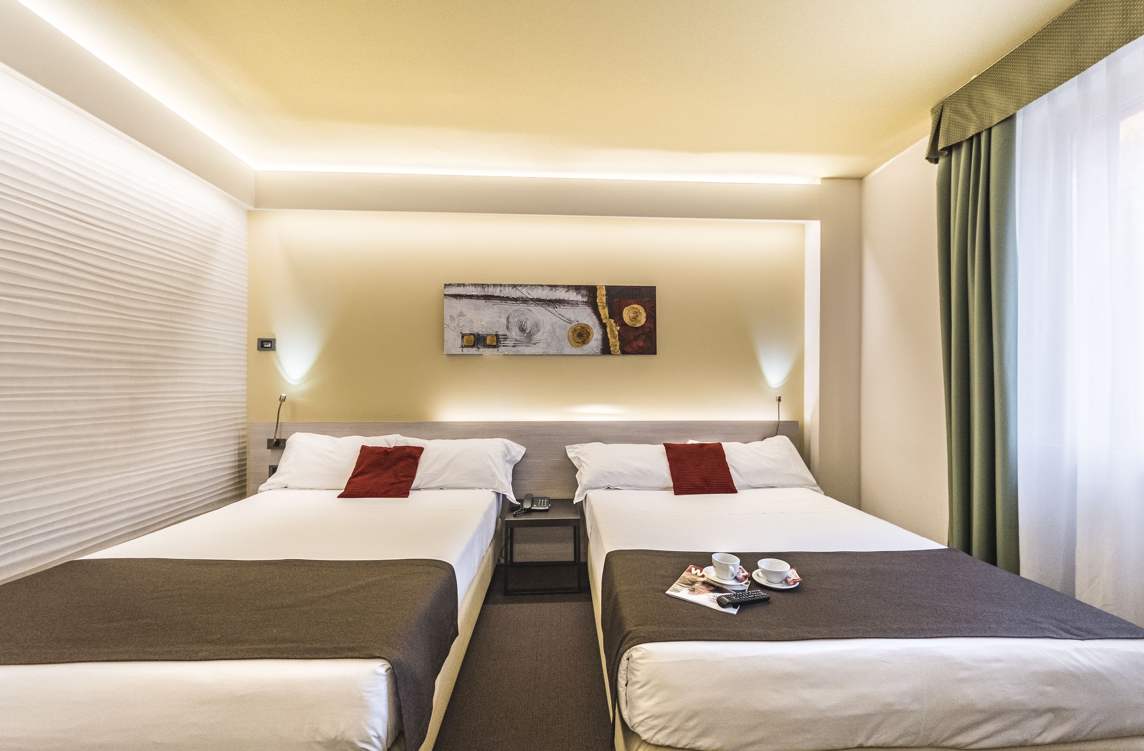 A hotel room with two beds, a small table, and a painting on the wall.