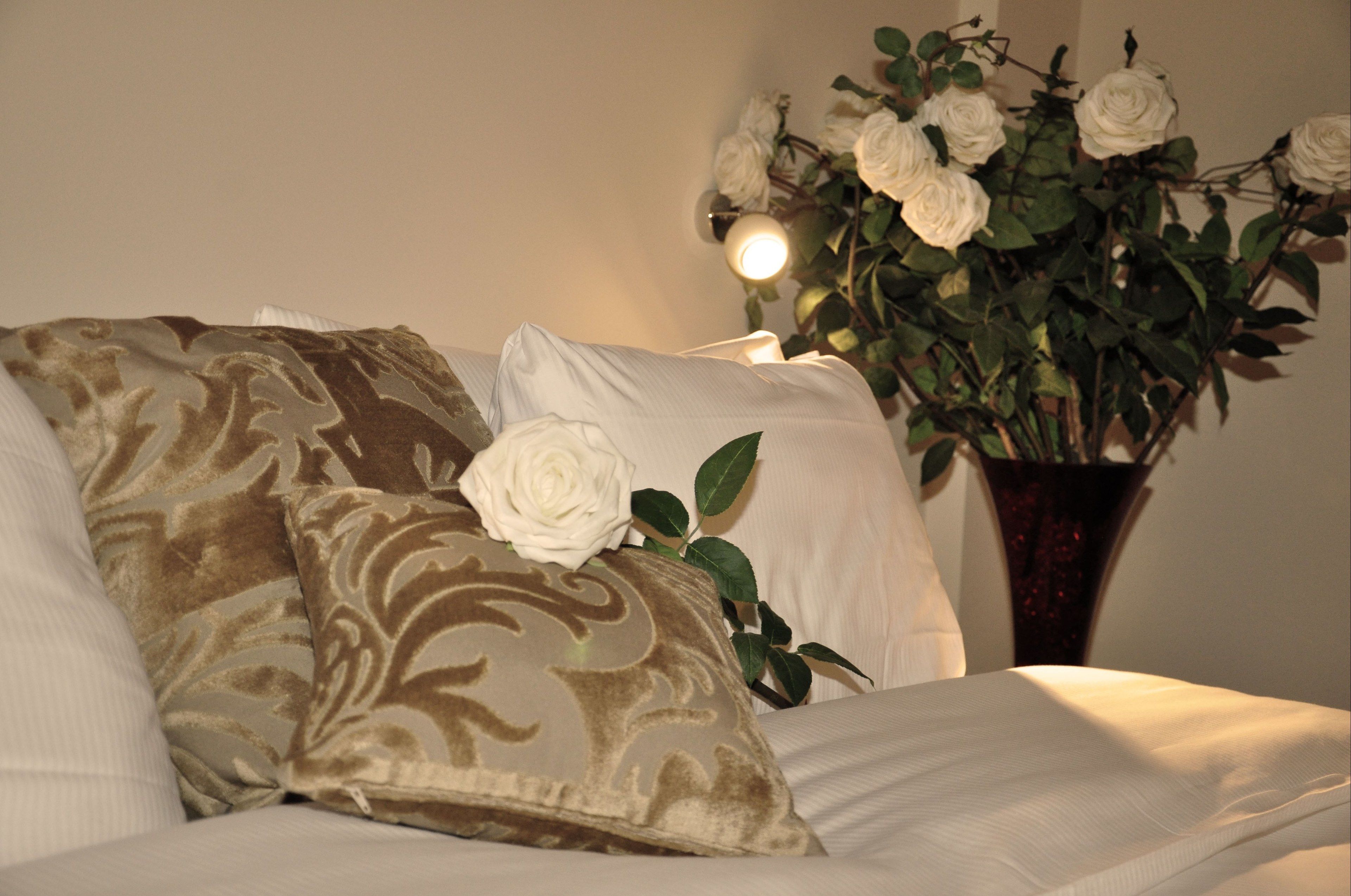 A bed with patterned pillows and a vase with white roses.