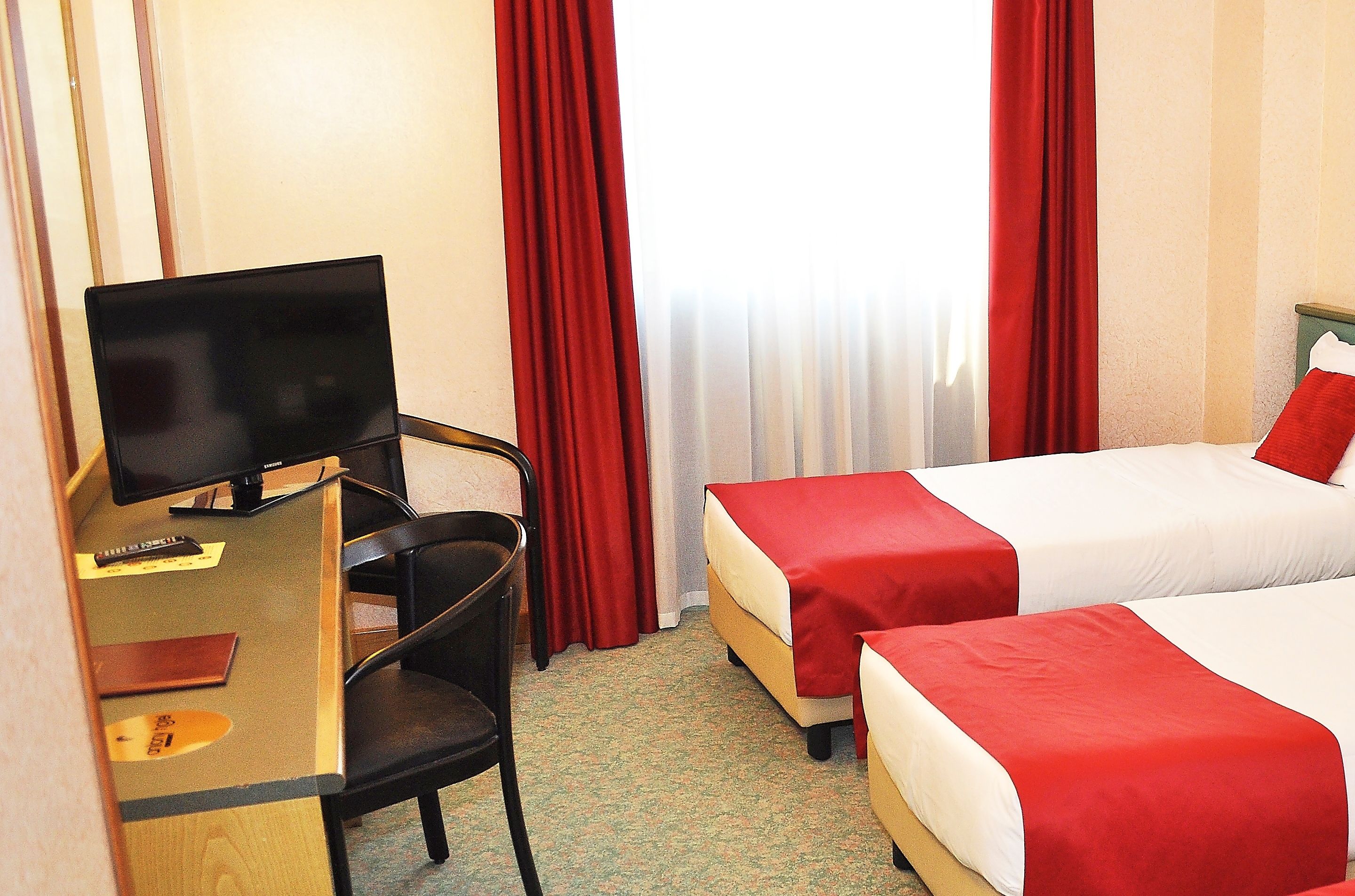 A hotel room with two beds, a desk, a chair, and a television.