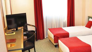 A hotel room with two beds, a desk, a chair, and a television.