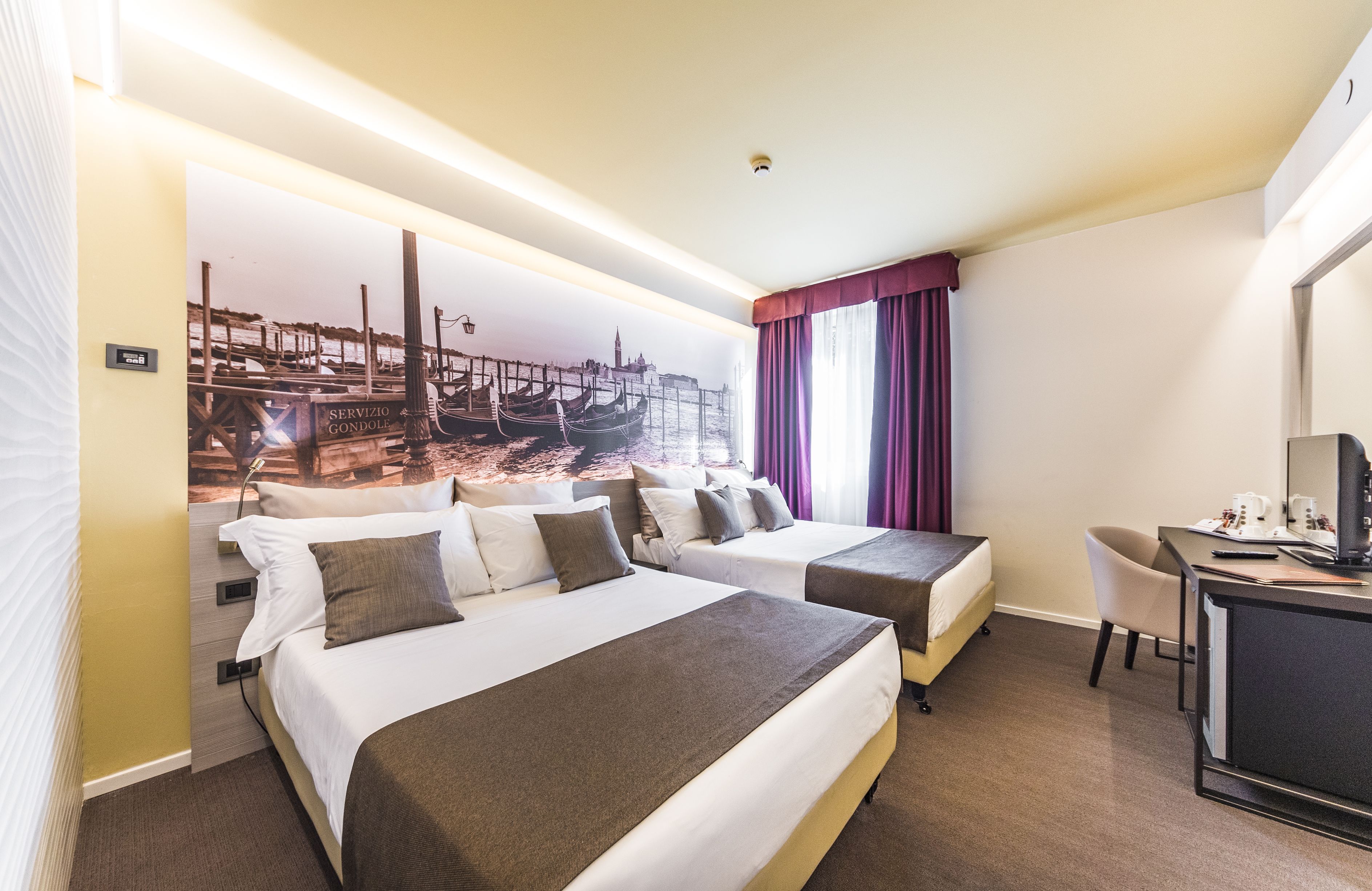Habitación de hotel con dos camas, un escritorio, una silla y un ventanal con cortinas.