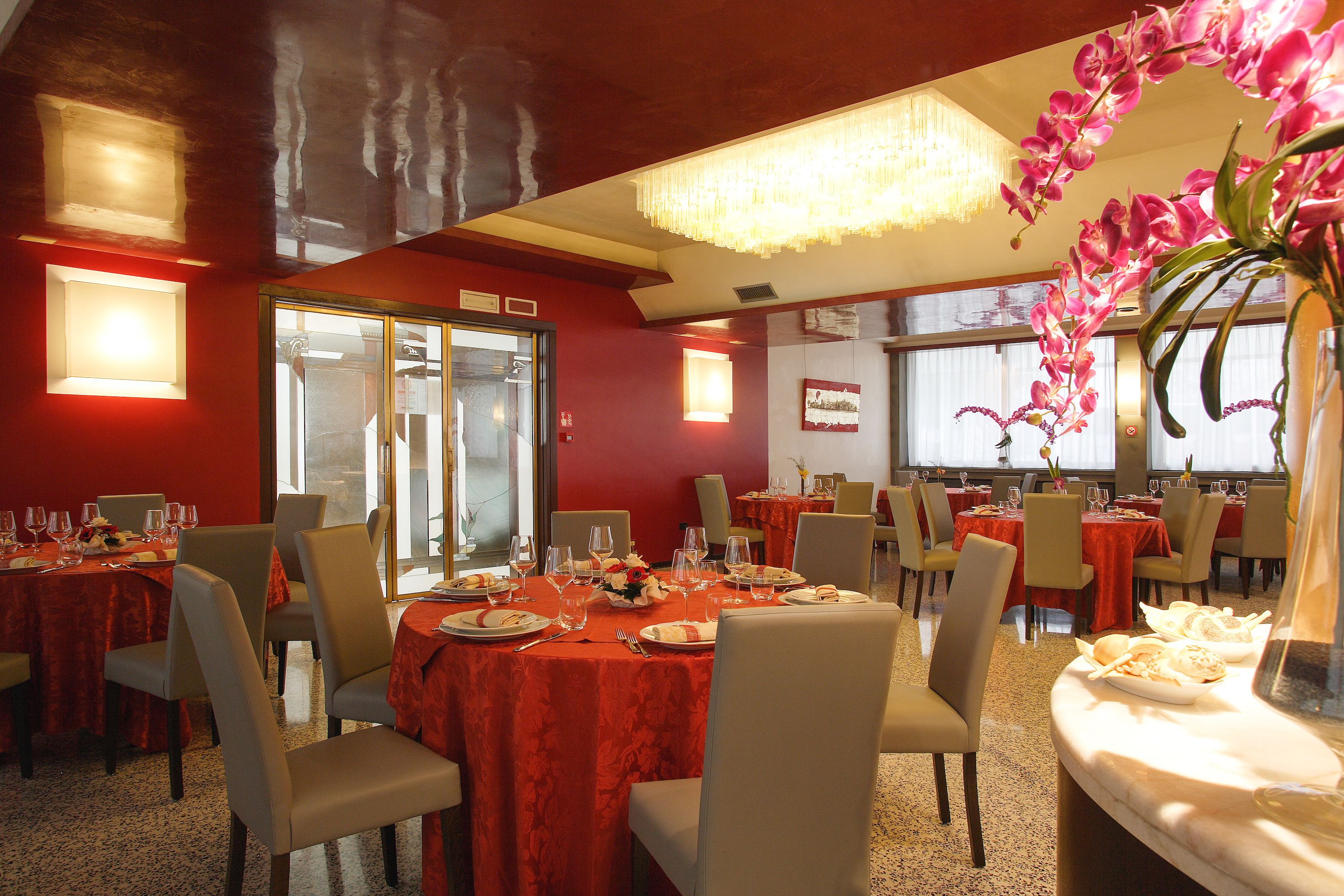 Un restaurante con manteles rojos, sillas blancas y una araña de cristal.