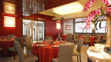 A restaurant with red tablecloths, white chairs, and a chandelier.