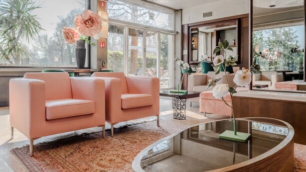 A modern living room with two peach-colored sofas, a glass coffee table, and a large window offering a view of trees and buildings. - Antony Hotel (Mestre)