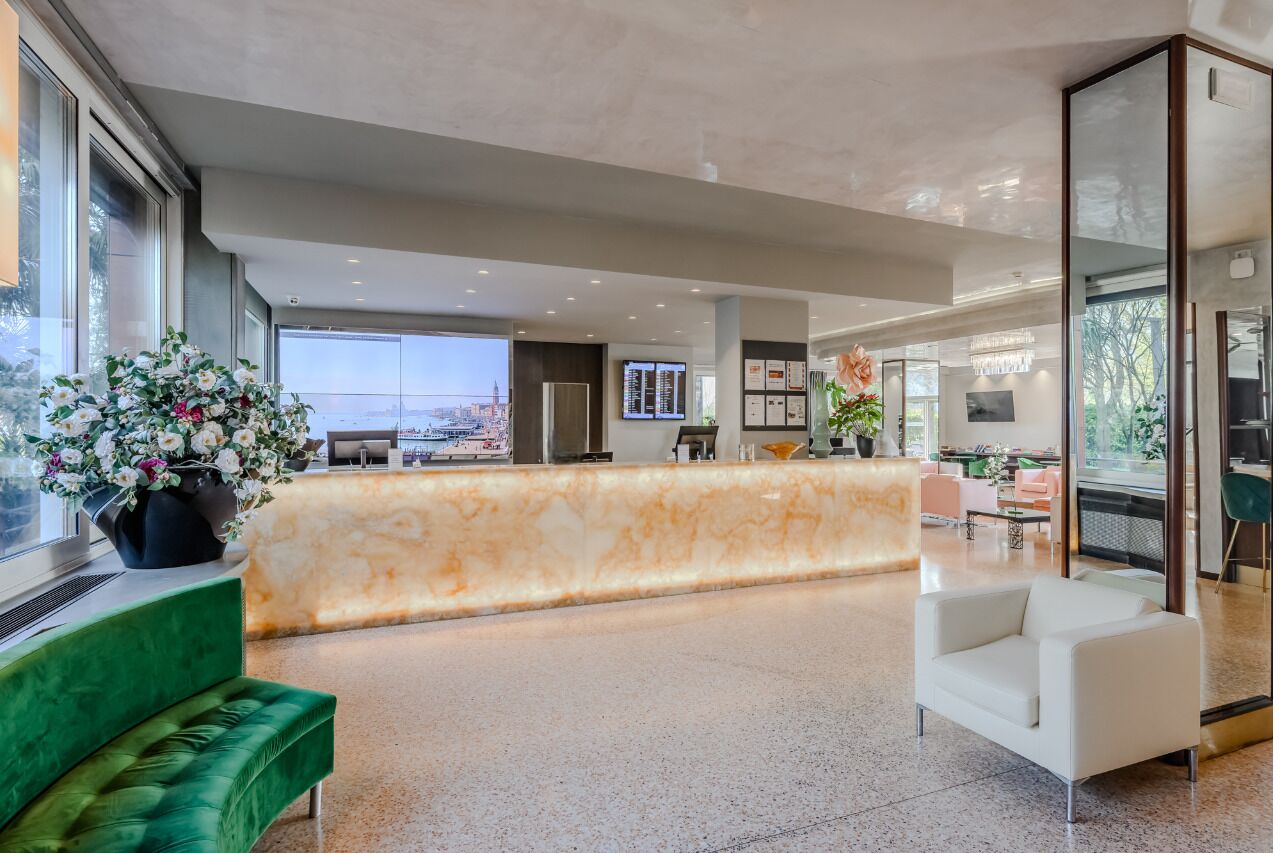 Un hall d’hôtel moderne avec un comptoir d’accueil en marbre, des sièges verts et une vue sur la ville.