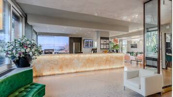 Un hall d’hôtel moderne avec un comptoir d’accueil en marbre, des sièges verts et une vue sur la ville.