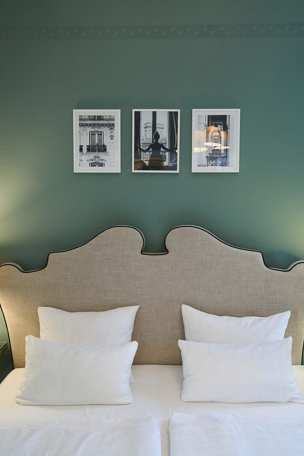 A bed with a headboard, two pillows, and three framed pictures on the wall.