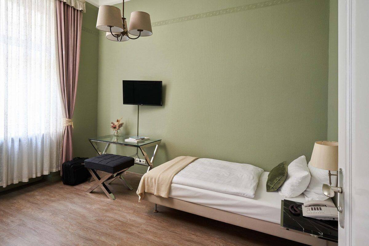 Une chambre d’hôtel avec un lit, une table de chevet, une lampe, une télévision et une fenêtre avec des rideaux.