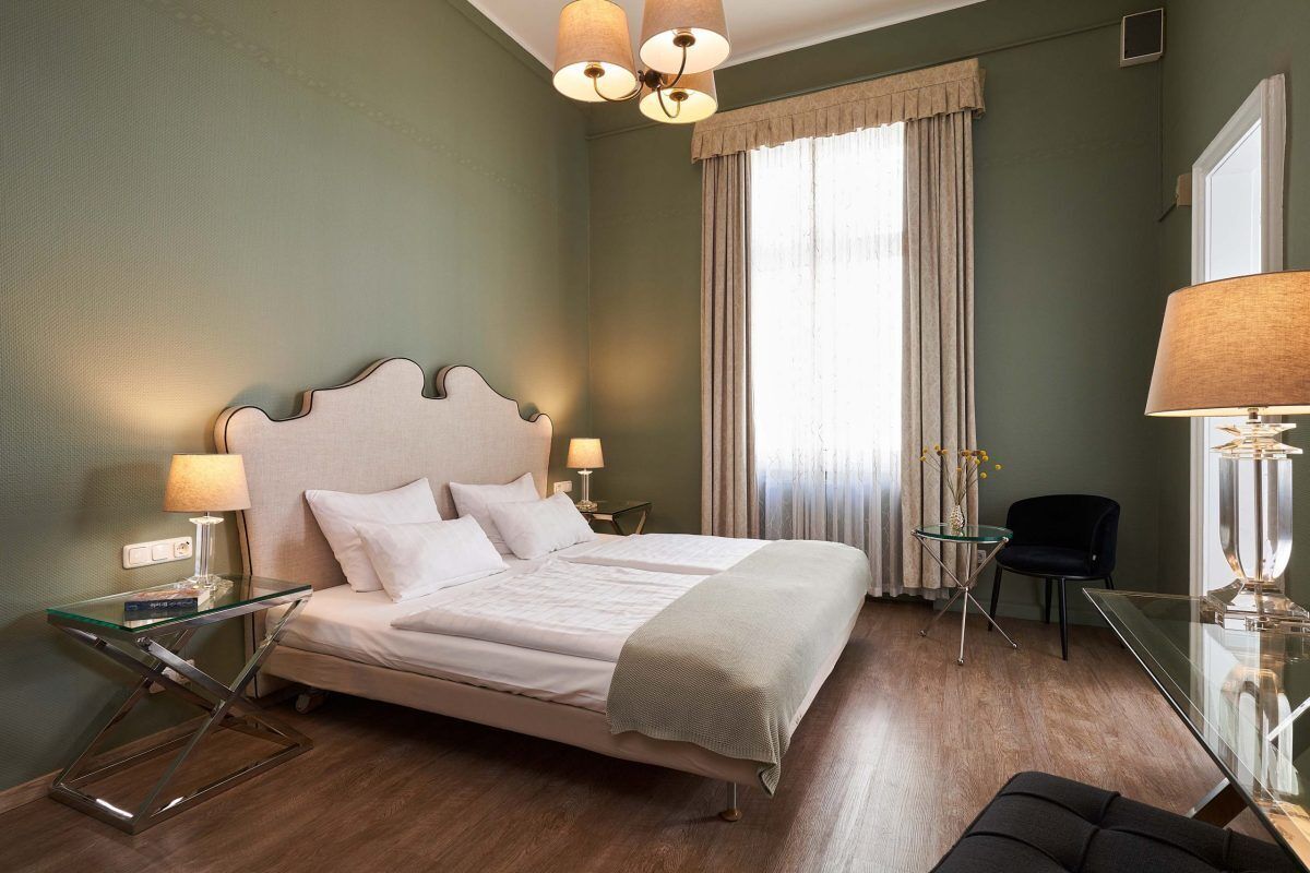 Ein ordentlich eingerichtetes Hotelzimmer mit Bett, Nachttischen, einem Sessel und einem Schreibtisch.