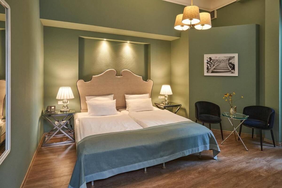 Une chambre à coucher avec un grand lit, deux tables de chevet avec des lampes, une petite table ornée de fleurs et deux chaises.