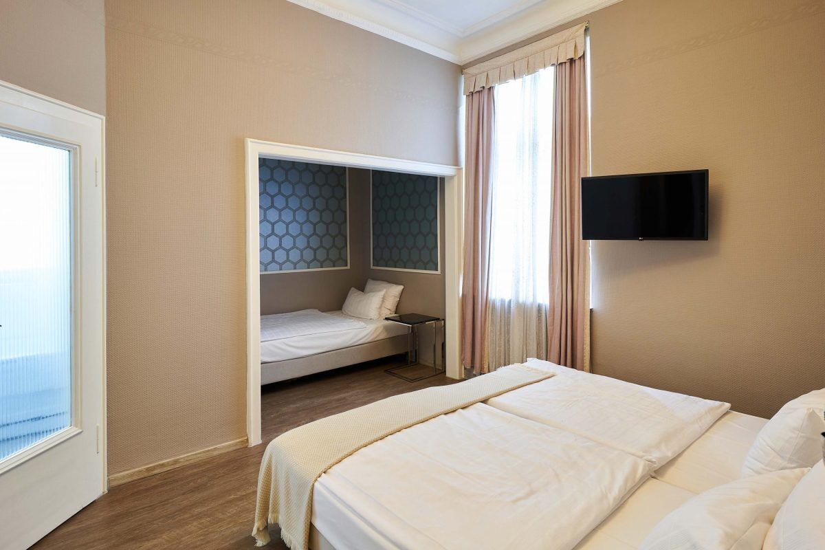 Ein Hotelzimmer mit einem großen Bett, einem kleineren Bett, einem an der Wand befestigten Fernseher und einem Fenster mit Vorhängen.