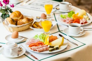 Una colazione con diversi cibi, tra cui pane, uova, formaggio e verdure, disposti su un tavolo con tovaglia bianca e righe verdi.