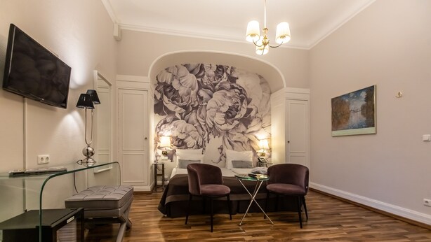 A hotel room with a large floral mural, a TV, a glass table, and two chairs.