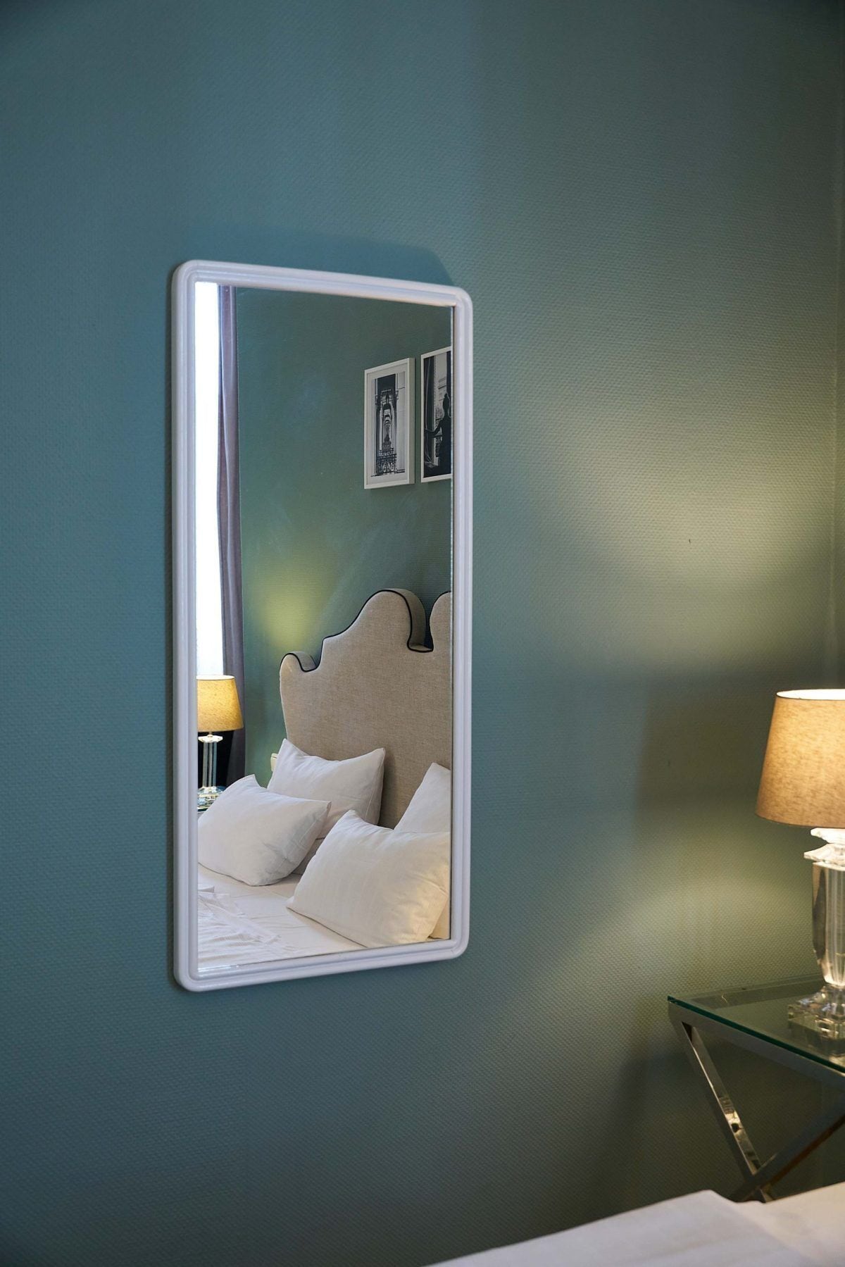 A bedroom with a bed, a nightstand, a lamp, and a mirror on the wall.