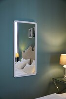 A bedroom with a bed, a nightstand, a lamp, and a mirror on the wall.