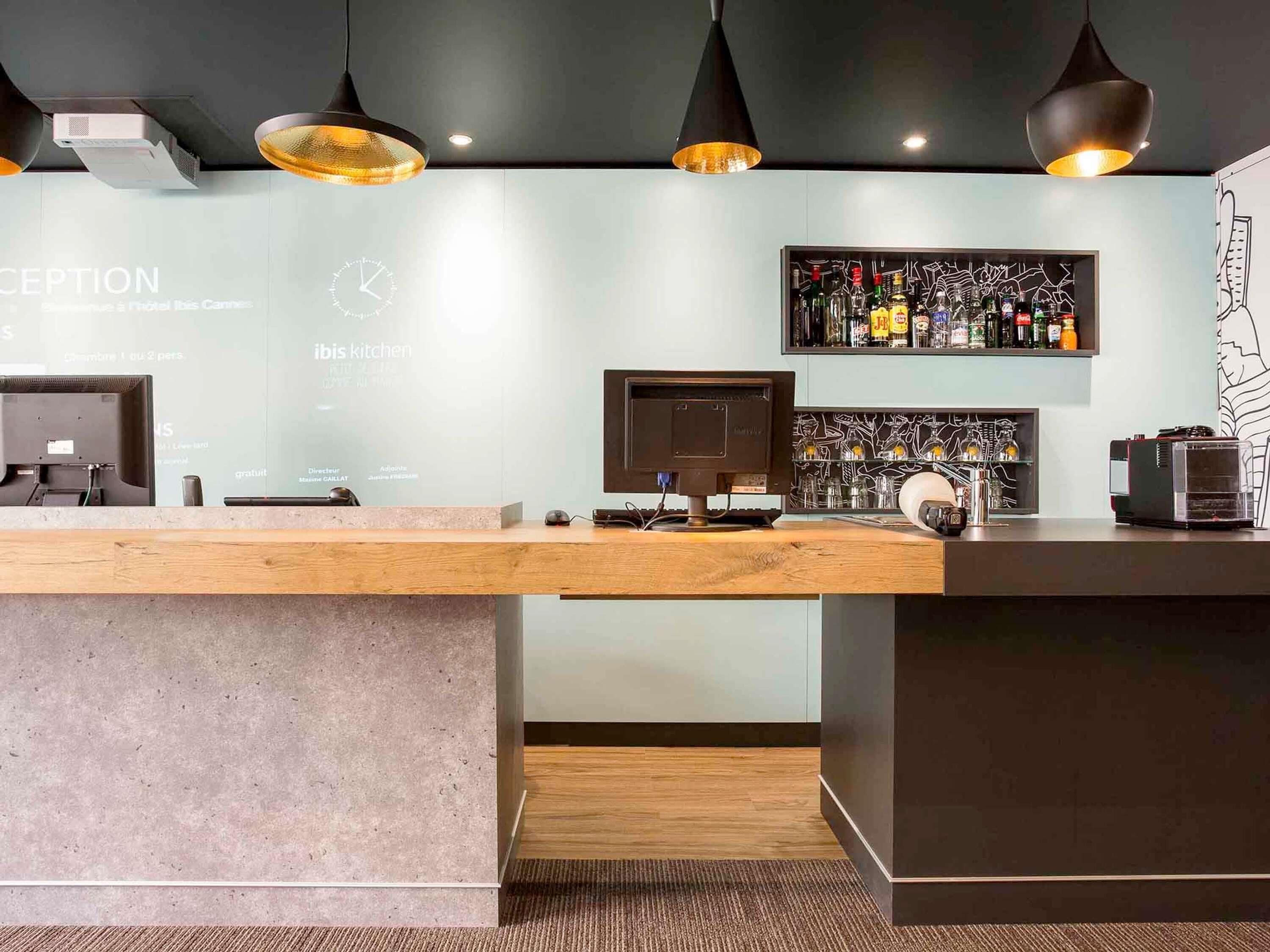 A reception desk with a computer, a clock, and a wall-mounted liquor display.